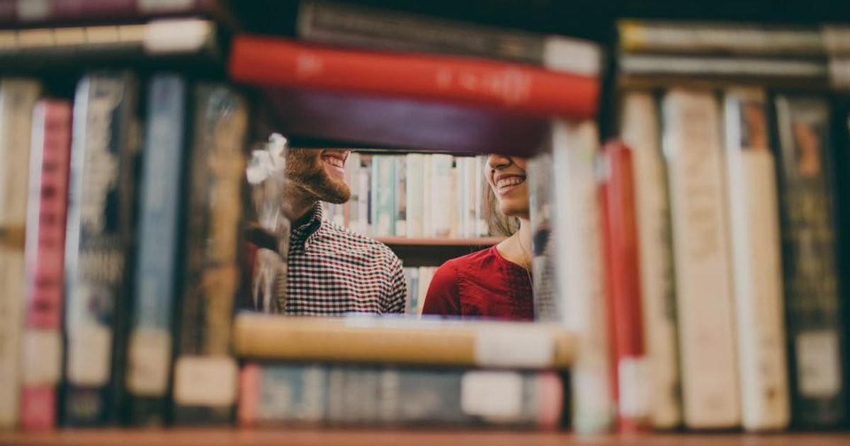 Students between library shelves reviewing study material together