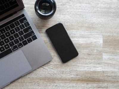 Smartphone beside a laptop and camera lens on a desk for a phone storage cleanup guide