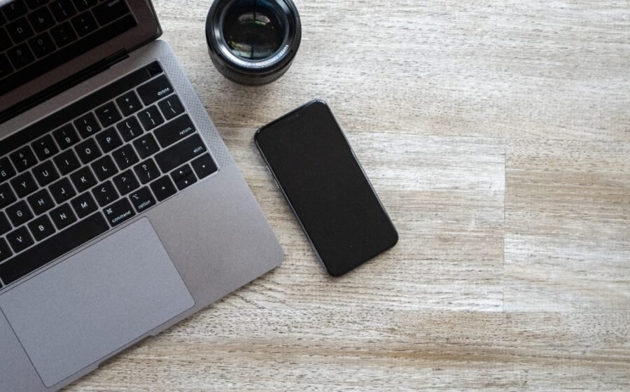 Smartphone beside a laptop and camera lens on a desk for a phone storage cleanup guide