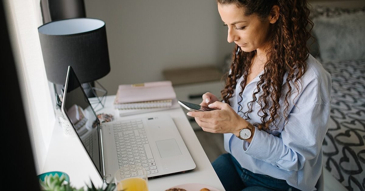 Person using a smartphone beside a laptop before backing up files