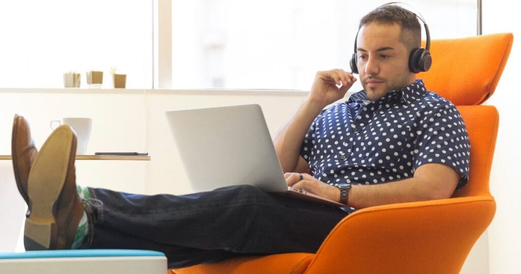 Man wearing over-ear headphones while working on a laptop in an orange armchair