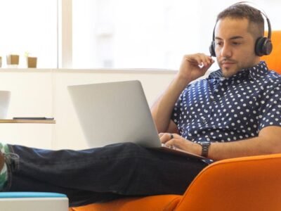 Man wearing over-ear headphones while working on a laptop in an orange armchair