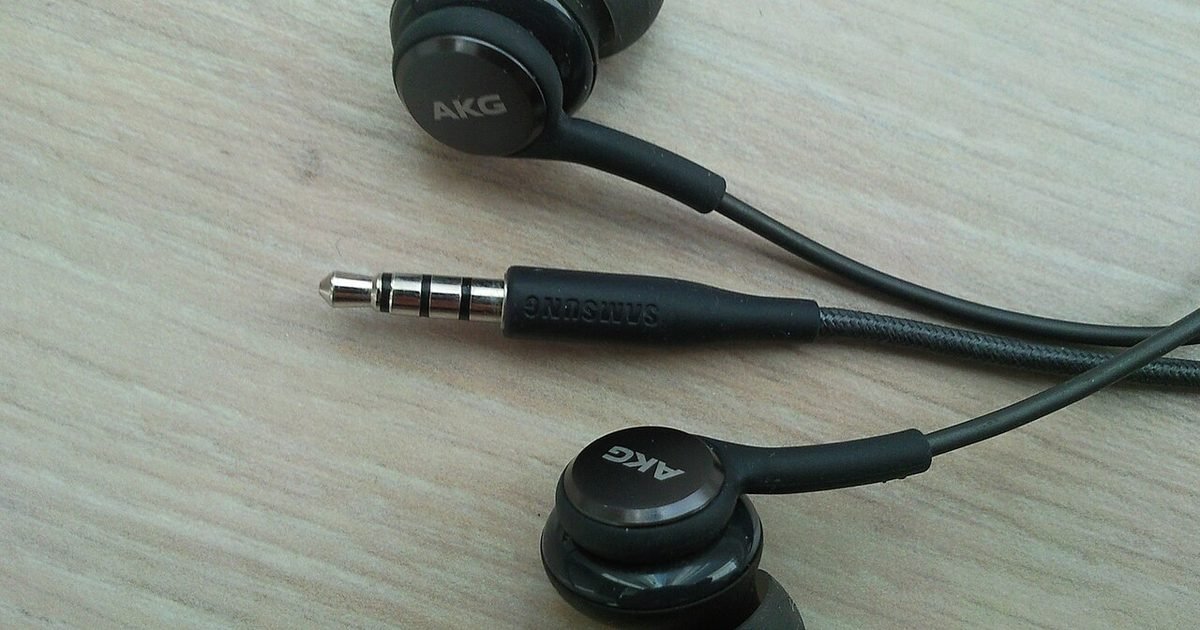 Close-up of wired AKG earbuds and a four-pole 3.5 mm audio plug on a wooden table