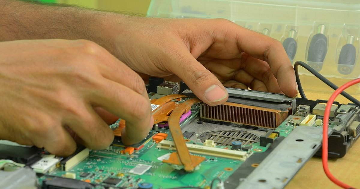 Hands repairing the inside of a laptop, illustrating repair risk and professional help.